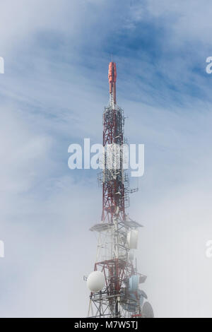 Antenne Getriebe Telecommunication Tower auf einem Berge im Nebel mit blauen Himmel hinter Stockfoto