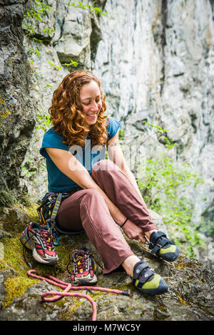 Das Porträt einer jungen Frau an einem Klettern Klettergarten, als sie ihre Schuhe Änderungen und macht sich bereit, um zu klettern. Stockfoto