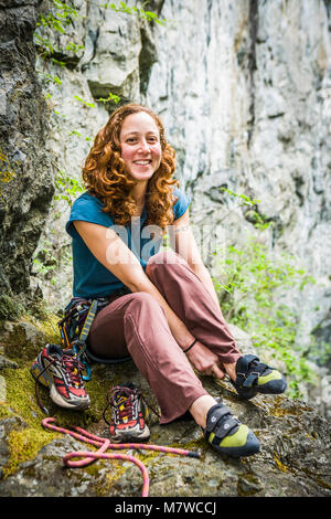 Das Porträt einer jungen Frau an einem Klettern Klettergarten, als sie ihre Schuhe Änderungen und macht sich bereit, um zu klettern. Stockfoto