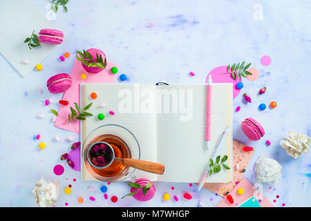 Weibliche Schriftsteller Arbeitsplatz mit einem offenen Notepad oder Tagebuch. Bunten süßen Snacks, Hard Candy, und Rosa macarons auf einem hellen Hintergrund mit Kopieren s Stockfoto