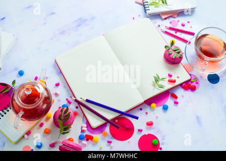 Feminine Hintergrund mit Tee, rosa Süßigkeiten, Bonbons, Konfetti und offenes Buch mit leeren Seiten. Bunte Planung party Konzept mit kopieren. Stockfoto