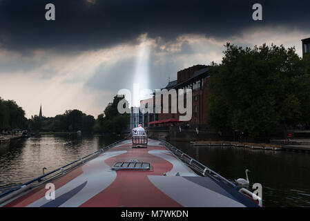 Mann saß auf der Vorderseite des Bootes mit der Welle des himmlischen Licht Streaming durch Sturm Cloud gewählt Stockfoto