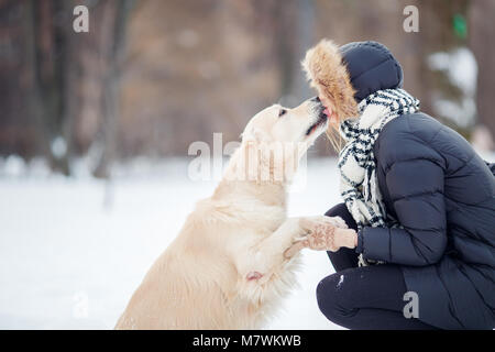 Bild von Mädchen umarmt Labrador in Snowy Park Stockfoto