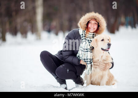 Bild von Mädchen in schwarzen Jacke hocken neben Hund im Winter Stockfoto