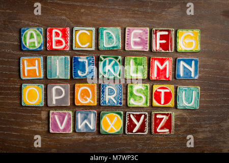 Farbenfrohe handgefertigte Keramik Alphabet auf Holz Textur Stockfoto