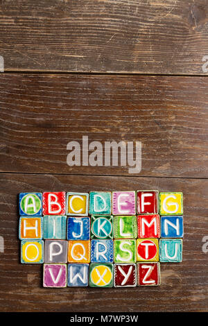 Farbenfrohe handgefertigte Keramik Alphabet auf Holz Textur Stockfoto