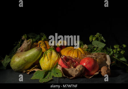 Eine Gruppe von typischen landwirtschaftlichen Produkte der Herbst (Kürbisse, Birnen, Walnüsse, Granatäpfel, Erdbeerbäumen, Mais) auf einem schwarzen Hintergrund mit einem Streiflicht. Stockfoto