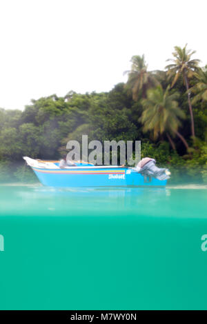 Ein Mann mit Sonnenbrille auf kleine blaue Boot an den ruhigen Gewässern des Atlantik in der Nähe der Fidschi-Inseln. Palmen und Bäumen im Hintergrund. Die Yacht engi Stockfoto