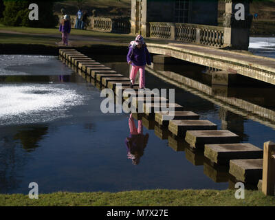 Zwei Kinder cross Trittsteine über zugefrorene See im Winter in Großbritannien Stockfoto