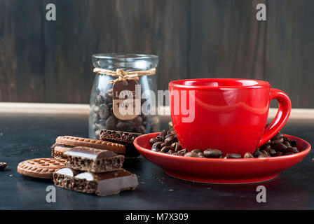 Rote heiße Tasse starken Kaffee mit Schokolade Cookies und Stücke von dunkler Schokolade und Kaffee Bohnen auf schwarzem Hintergrund Stockfoto