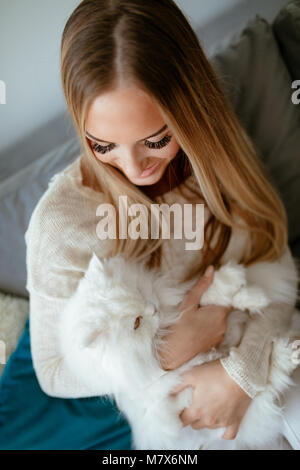 Nette junge Frau zu Hause entspannen und umarmt ihre schönen weißen Perser Katze. Stockfoto