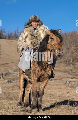 Mongolische Mann mit einem Wolf haut Jacke, reiten sein Pferd in einer Steppe im Norden der Mongolei Stockfoto