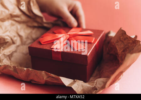 Das Mädchen hat ein Geschenk in einem schönen roten Kasten mit einem Band erhalten und wird, um es zu öffnen. Glückliches Ereignis. Stockfoto