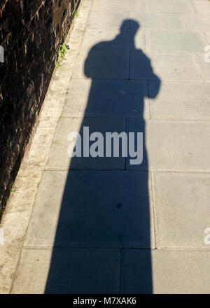 Langer Schatten der Figur auf der Straße in hellem Sonnenlicht Stockfoto