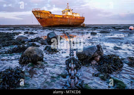 Rostigen alten Fischereifahrzeuges marooned bei Ebbe auf einer Schlamm Bank die Boote lange große Anker Kette vom mittleren Vordergrund geht an das Boot im backgro Stockfoto