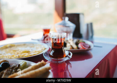 Close-up: Eine heiße Tasse duftenden schwarzen Tee. Zwei Platten mit vegetarischem Essen - frisches Gemüse und Käse, Kuchen und Getränke in Glas Rot, Tabelle Stockfoto