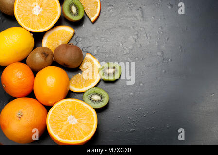 Vielzahl von frischen Zitrusfrüchten auf dunklem Hintergrund aus Schichten von Kiwi und Orangen, kopieren Raum Stockfoto