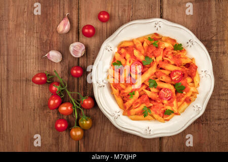 Ein Foto von einem Teller Pasta mit Tomatensauce. Penne Rigate mit Cherry Tomaten und frische Petersilie, mit Zutaten, auf eine dunkle Tropfen Stockfoto