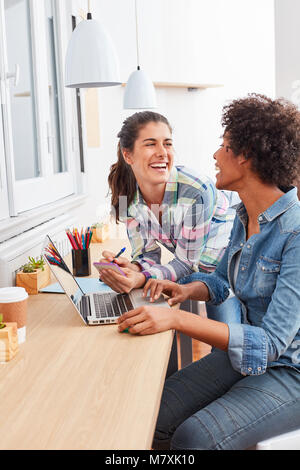 Zwei junge Frauen als Kolleginnen und Kollegen arbeiten und zusammen lachen auf Laptop Stockfoto