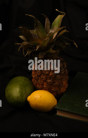 Ananas, Mango, Zitrone und Buch auf schwarzem Hintergrund. Stockfoto