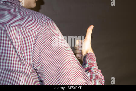 Der junge Mann drehte sich weg und zeigt die Zeichen OK, die Finger nach oben, Schatten an der Wand. Stockfoto