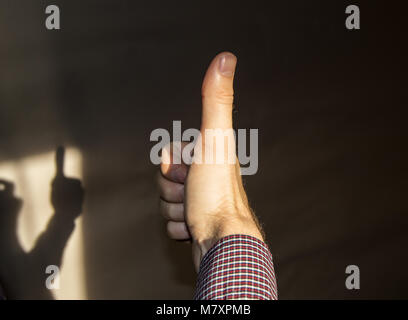 Der junge Mann drehte sich weg und zeigt die Zeichen OK, die Finger nach oben, Schatten an der Wand. Stockfoto