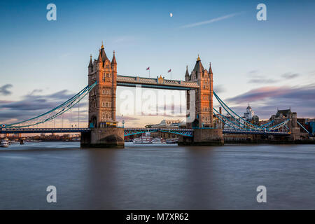 LONDON, UK-NOV 2017: London's Iconic Tower Bridge bei Sonnenuntergang mit einem halben Mond über es und der Themse im Vordergrund. Stockfoto