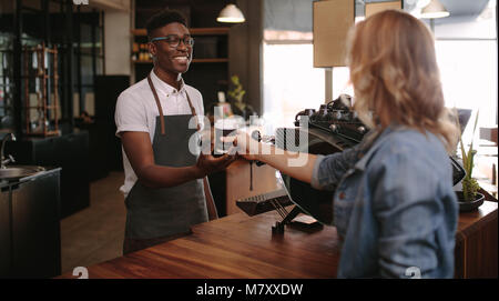 Coffee shop besitzer Übergabe einer versiegelten Kaffeetasse zu einem Kunden. Mann, das Kunden mit einem Lächeln im Coffeeshop. Stockfoto