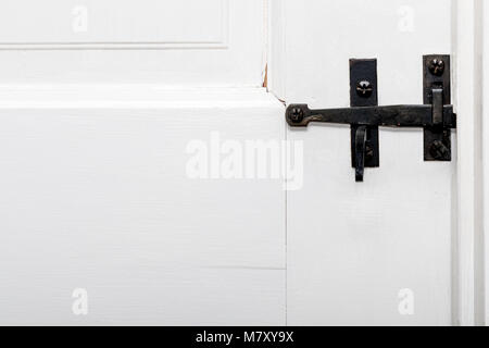Eine antike schwarzen schmiedeeisernen Tür Verriegelung auf eine weiße Tür lackiert bewaldet.