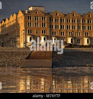 Hotels beleuchtet von der aufgehenden Sonne in feuchten Sand reflektiert an der Küste von Llandudno, North Wales Küste Stockfoto