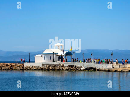 Sommer in Griechenland. Die Menschen warten auf das Brautpaar außerhalb von einem griechischen traditionellen weißen kleinen Kapelle am Meer und unter einem klaren blauen Himmel Stockfoto