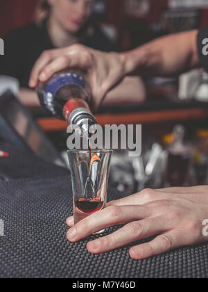 Der Barkeeper gießt Alkohol in ein Glas auf der Theke Stockfoto