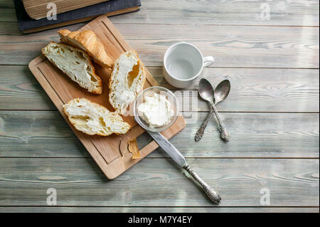 Frisch gebackene Croissants mit Butter auf einem Schneidebrett auf einem Holztisch. Frühstück Konzept. Ansicht von oben Stockfoto