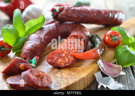 Spanische Salami: würzige Chorizo Wurst mit Tomaten und Basilikum auf einem Schneidebrett Olivenholz serviert. Stockfoto