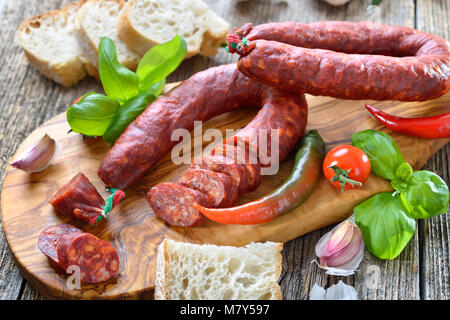 Spanische Salami: würzige Chorizo Wurst mit Tomaten und Basilikum auf einem Schneidebrett Olivenholz serviert. Stockfoto