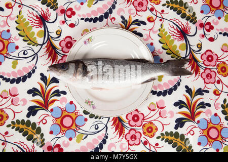 Eine Baß-Fischen im Inneren eine Blume Platte auf einem geblümten Stoff versteckt. Camouflage Spiel. Minimale Farbe still life Fotografie. Stockfoto
