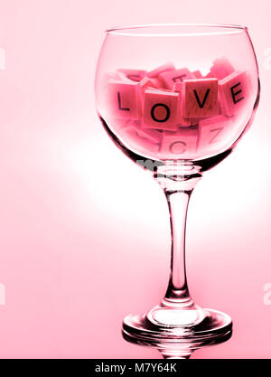 Ein großes Glas Wein mit den Worten der Liebe in Scrabble Buchstaben, mit roten Farbstich Stockfoto