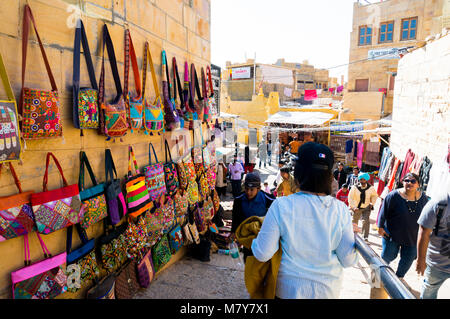 Jaisalmer, Indien - 28 Dez 2018: Menschen zu Fuß durch die Gassen der Golden Fort in Jaisalmer, während an der schönen Handwerk Taschen hängen an den Wänden. Dieses lebendige Fort hat viele kleine Anbieter, die Waren auf den Straßen und Wänden zur Schau zu stellen, zu den Touristen. Stockfoto