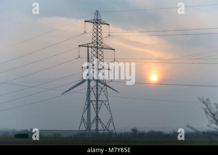 Wind Turbine und Strom pylon bei Sonnenuntergang Stockfoto