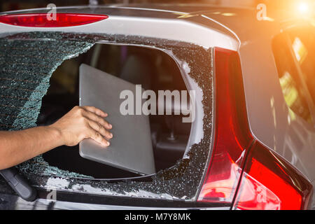 Nahaufnahme der Hand stehlen Laptop von der Rückseite der Auto, das hintere Glas gebrochen Stockfoto