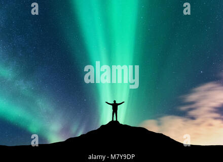 Aurora und Silhouette der stehende Mann mit erhobenen Armen auf dem Berg. Lofoten, Norwegen. Aurora borealis und glücklicher Mensch. Himmel mit Sternen und Stockfoto