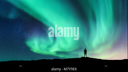 Aurora borealis und Silhouette der stehende Mann. Lofoten, Norwegen. Aurora und glücklicher Mensch. Himmel mit Sternen und grüne Polarlichter. Nacht Landschaft Stockfoto