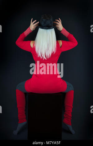 Eine reife Frau, in einer abstrakten künstlerischen Stil zurück zur Kamera posieren, das Tragen der roten Pullover und Beinlinge, graue Socken und Leggings einen Hut tragen. Stockfoto