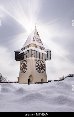 Sun flares über verschneite Uhrturm Uhrturm Wahrzeichen der Stadt Graz auf Hill Schlossberg im Winter Stockfoto