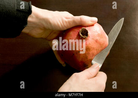 Nahaufnahmen der Hände Aufschneiden ein Granatapfel mit einem Edelstahl Messer - der dunkle Hintergrund mit Kopie Raum Stockfoto