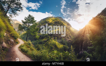 Erstaunliche Szene mit Himalaya grünes Gras und Bäumen bedeckt, blau bewölkten Himmel mit Sonne, Wolken und schönen Weg in Nepal bei Sonnenuntergang. Panorami Stockfoto