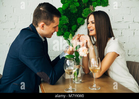 Fröhlicher junger Mann und Frau sind dating im Restaurant. Sie sitzen am Tisch und an einander mit der Liebe. Stockfoto