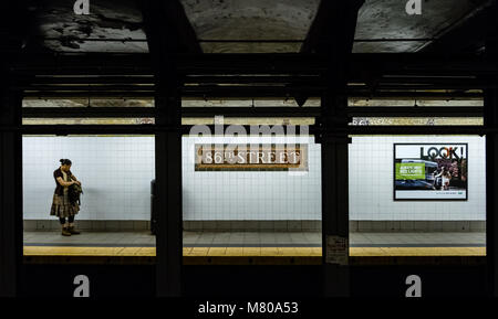 Eine Frau sieht in ihrem Beutel während der Wartezeit für einen Zug auf der U-Bahn-Station 86th Street, Manhattan, New York City Stockfoto