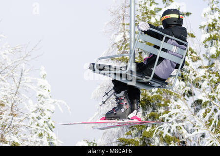 Person sitzen auf Skilift mit Schnee Bäume im Hintergrund Stockfoto