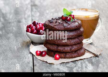 Stapel von dunkler Schokolade Cookies mit Cranberry und Tasse Kaffee auf Holz- Hintergrund Stockfoto